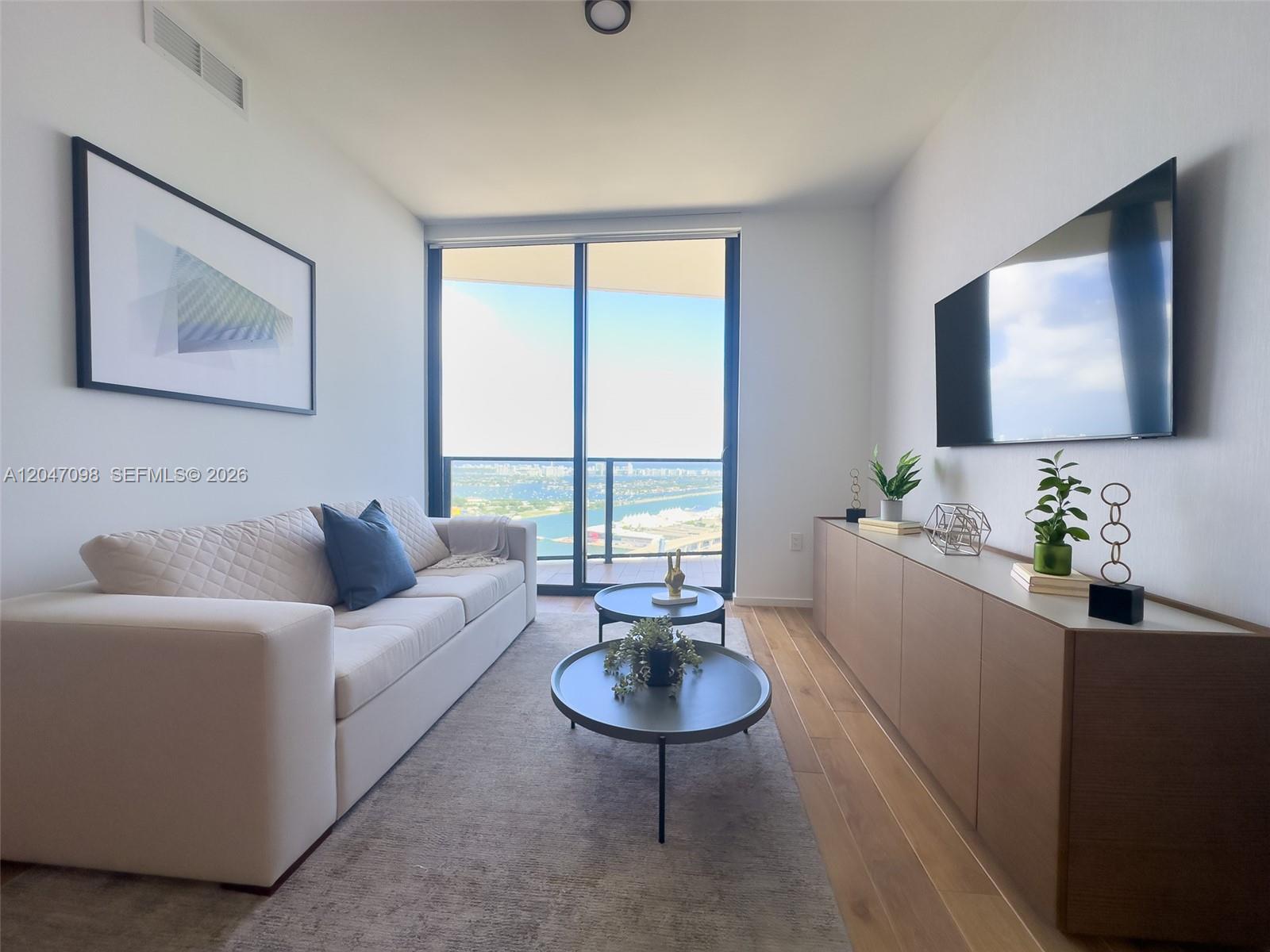 A modern living room features a white sofa, two round coffee tables, and a balcony view — 398 NE 5th St # 4210, Miami FL 33132, MIAMI, FL