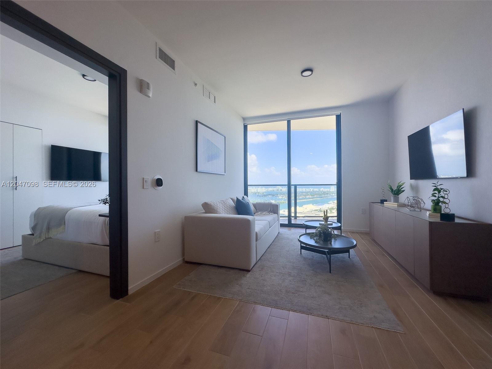 A living room with light wood floors, a beige sofa, and a view of the ocean — 398 NE 5th St # 4210, Miami FL 33132, MIAMI, FL