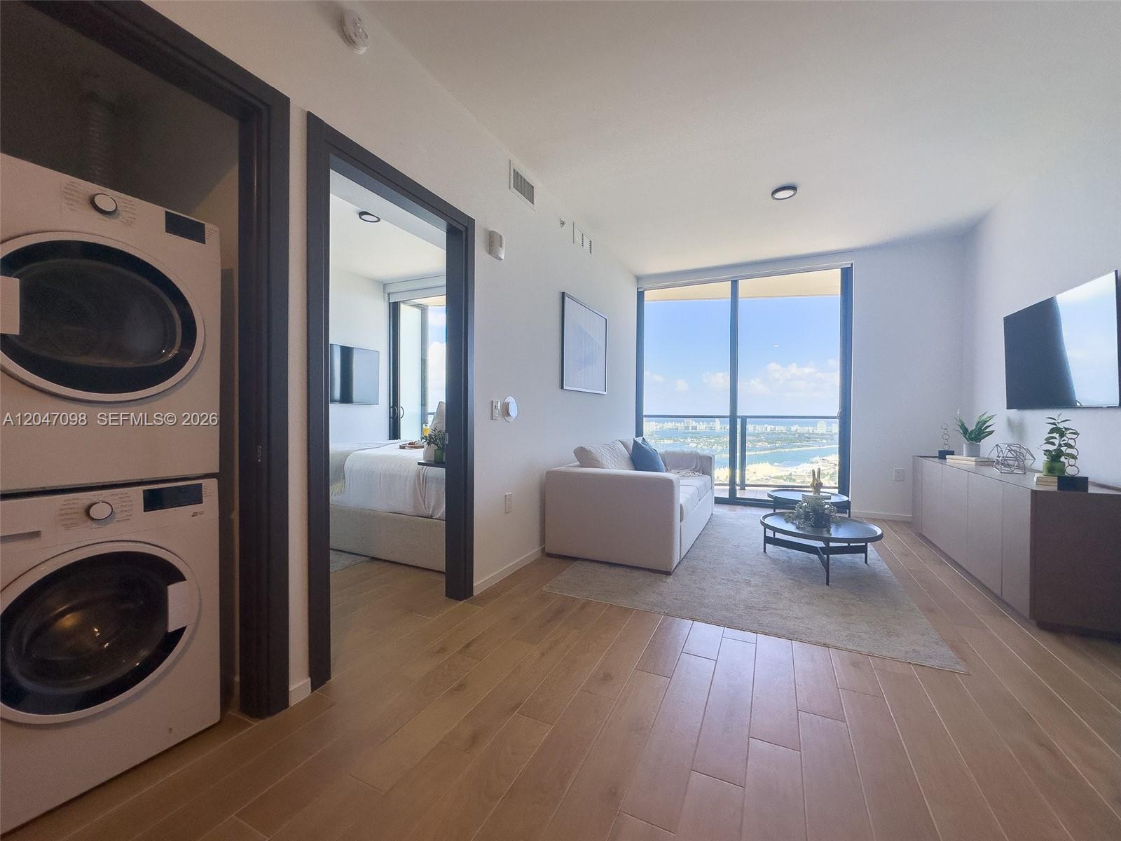 A living room with light wood floors, a stacked washer-dryer, and a balcony with water views — 398 NE 5th St # 4210, Miami FL 33132, MIAMI, FL