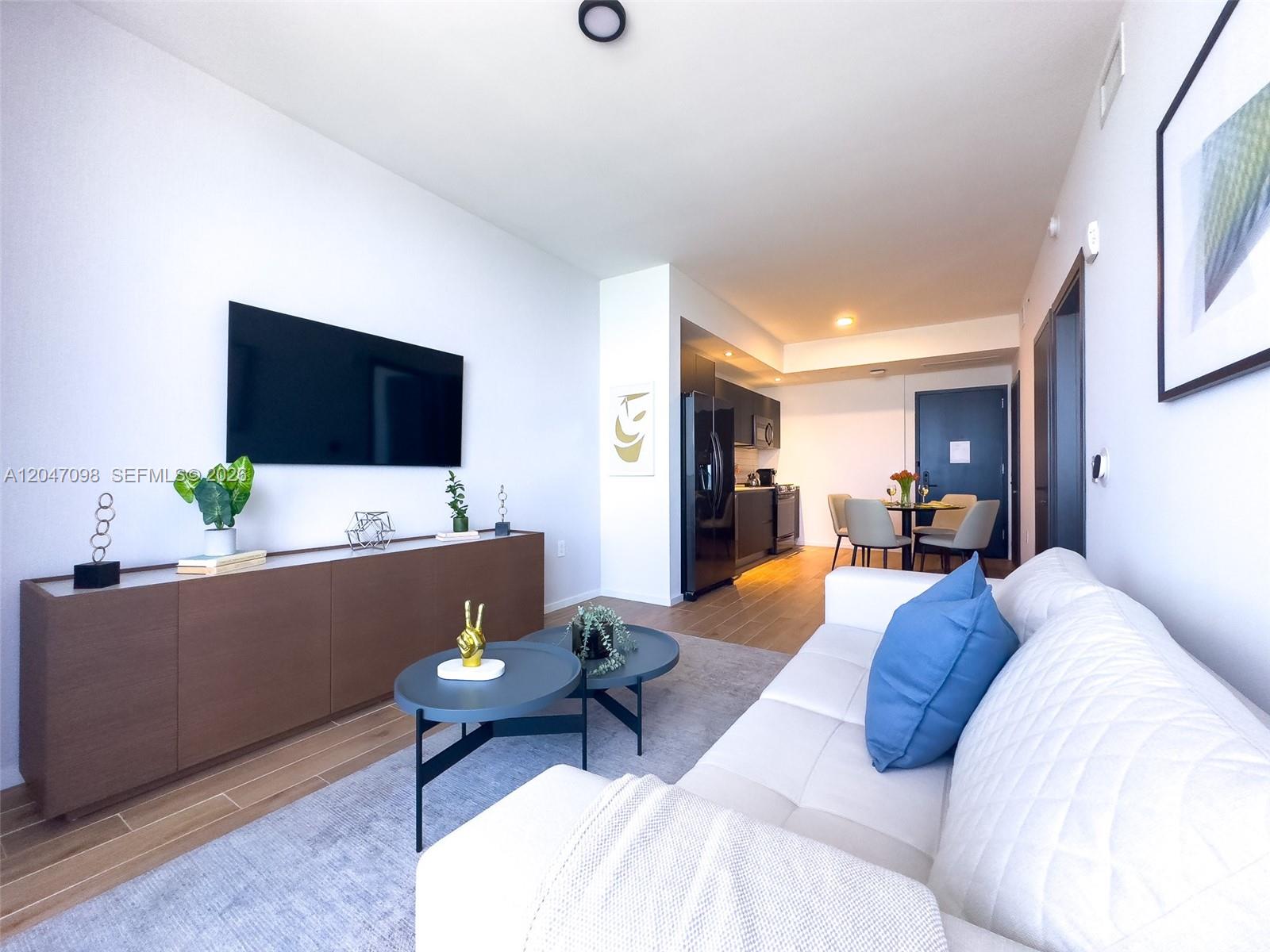 A modern living room features a white sofa, a television, and an adjacent kitchen area — 398 NE 5th St # 4210, Miami FL 33132, MIAMI, FL
