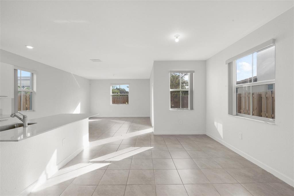 An open-concept kitchen and living area with white walls, tile flooring, and multiple windows — 2441 NW 131st Circle # 2441, Miami FL 33167, MIAMI, FL