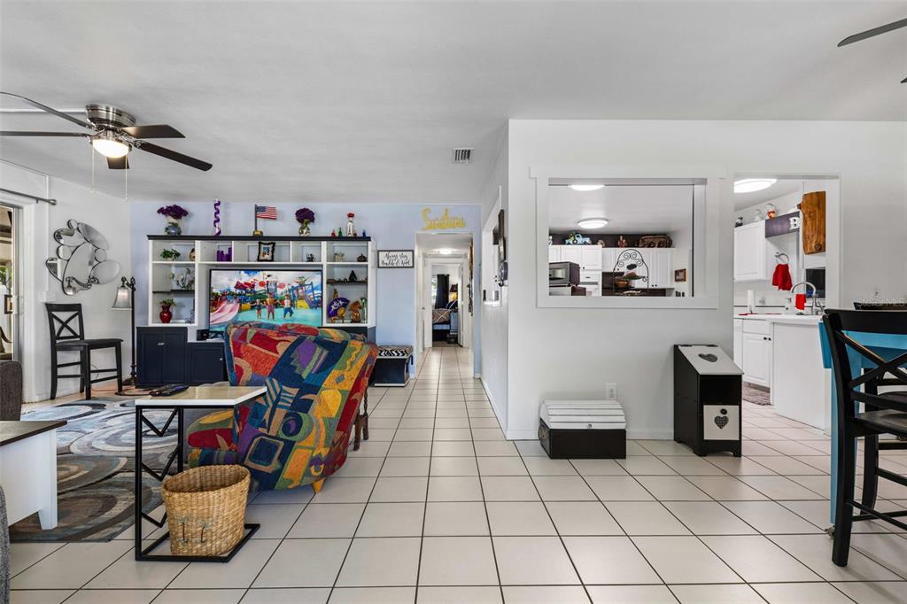 A living room with tiled floors, a colorful armchair, and a view into the kitchen — 936 AVENUE T SE, WINTER HAVEN, FL