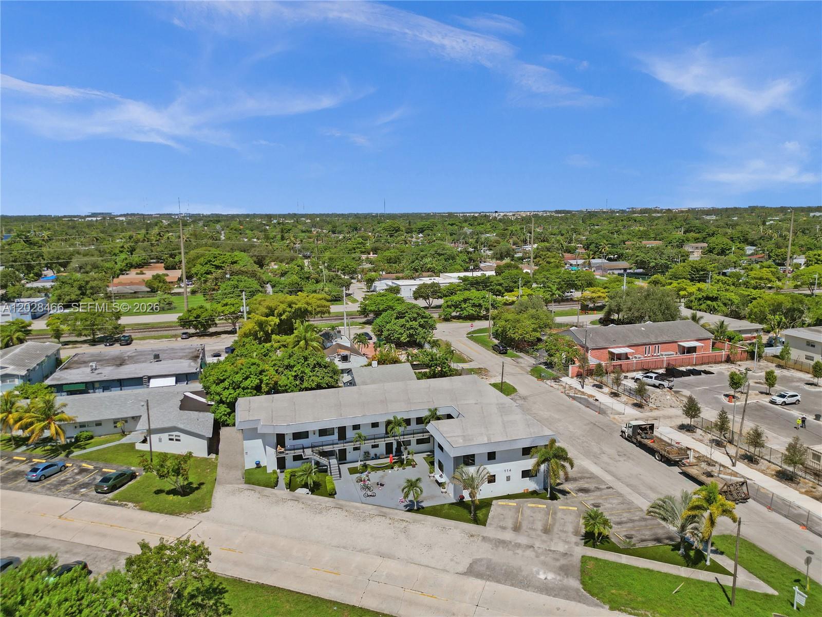An aerial view shows a two-story apartment building with a parking lot and surrounding greenery — 114 SE 8th St # 105, Hallandale Beach FL 33009, HALLANDALE BEACH, FL
