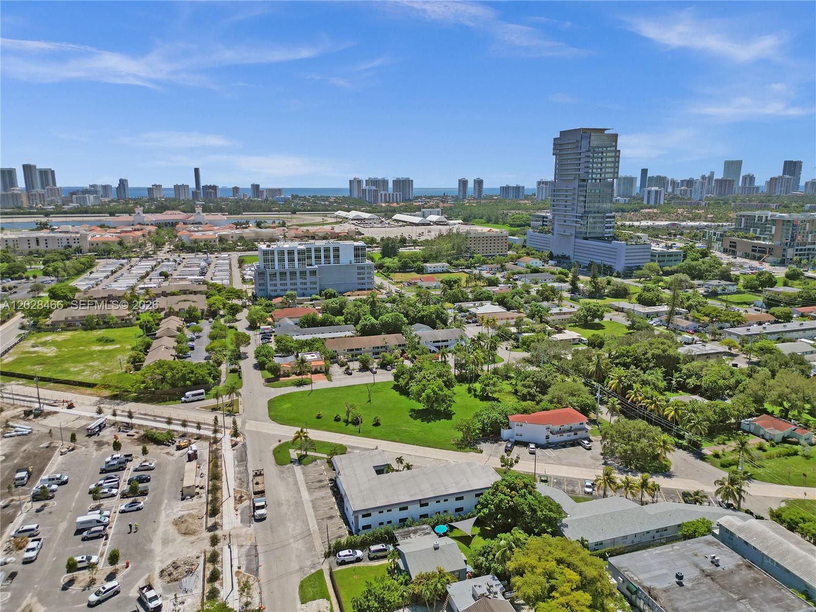 An aerial view shows a suburban neighborhood with low-rise buildings, green spaces, and distant skyscrapers — 114 SE 8th St # 105, Hallandale Beach FL 33009, HALLANDALE BEACH, FL