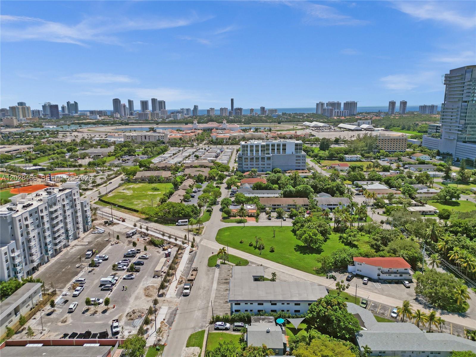 An aerial view shows a suburban neighborhood with parking lots, apartment buildings, and a distant skyline — 114 SE 8th St # 105, Hallandale Beach FL 33009, HALLANDALE BEACH, FL