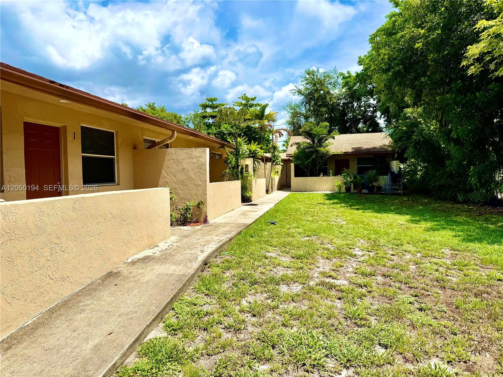 A concrete walkway leads past tan stucco residential units toward a grassy backyard area — 2227 Monroe St # 6, Hollywood FL 33020, HOLLYWOOD, FL