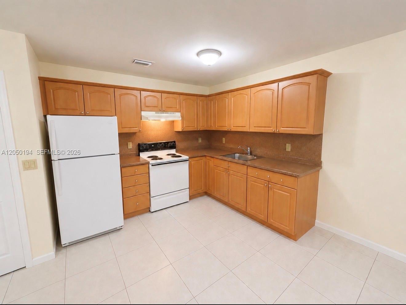 A kitchen features light wood cabinets, white appliances, and tan countertops over tiled flooring — 2227 Monroe St # 6, Hollywood FL 33020, HOLLYWOOD, FL