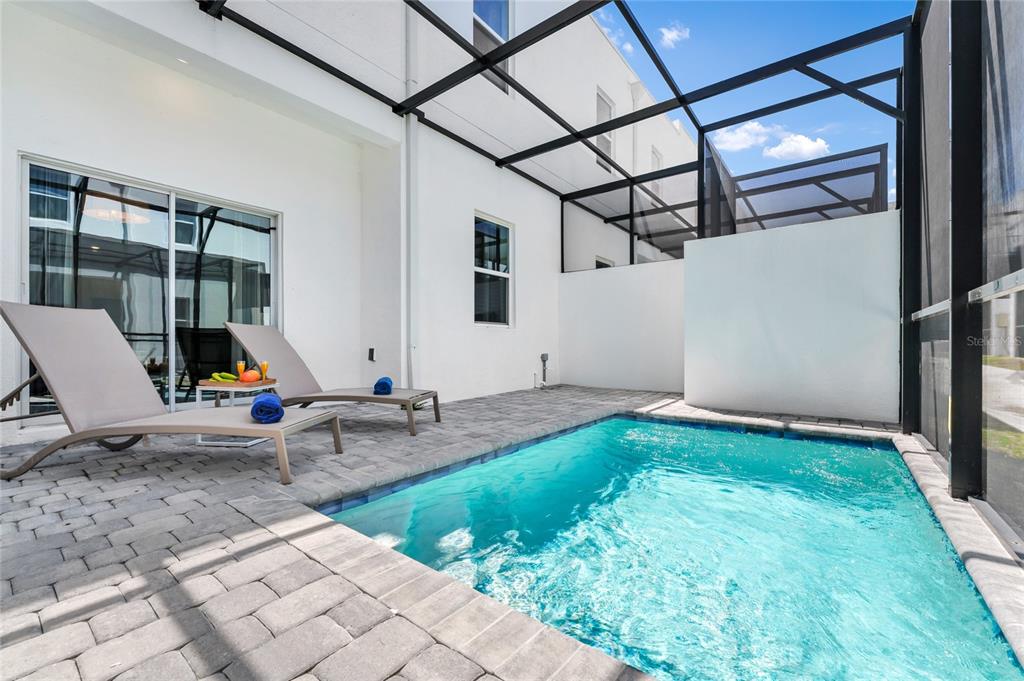 A small backyard swimming pool with a screened enclosure and two lounge chairs on pavers — 395 FAMAGUSTA DRIVE, DAVENPORT, FL