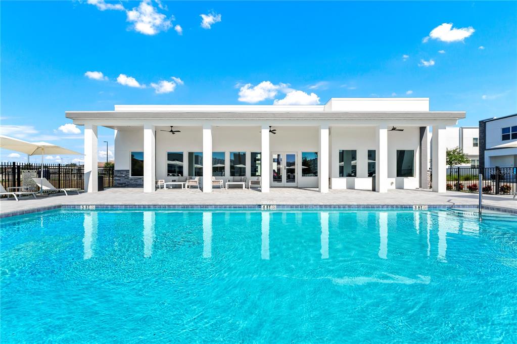 A swimming pool sits in front of a modern, white clubhouse with a covered patio — 395 FAMAGUSTA DRIVE, DAVENPORT, FL