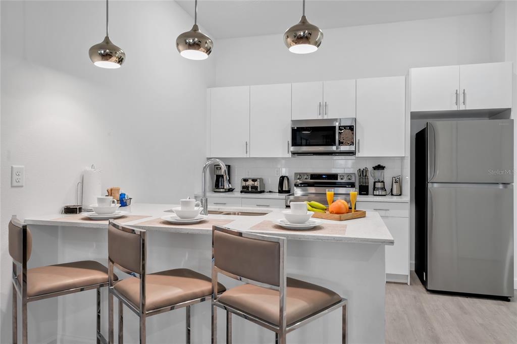 A modern kitchen features white cabinetry, stainless steel appliances, and a breakfast bar with stools — 395 FAMAGUSTA DRIVE, DAVENPORT, FL