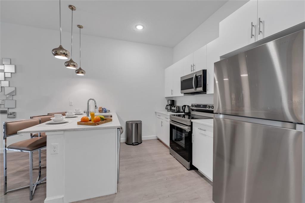 A modern kitchen features white cabinetry, stainless steel appliances, and a central island with seating — 395 FAMAGUSTA DRIVE, DAVENPORT, FL
