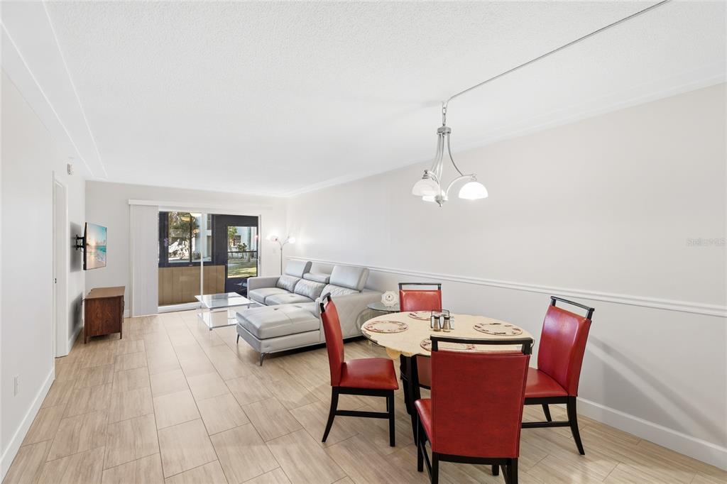 A living and dining area with light tile flooring, a grey sectional, and red chairs — 2300 STICKNEY POINT ROAD UNIT 102, SARASOTA, FL