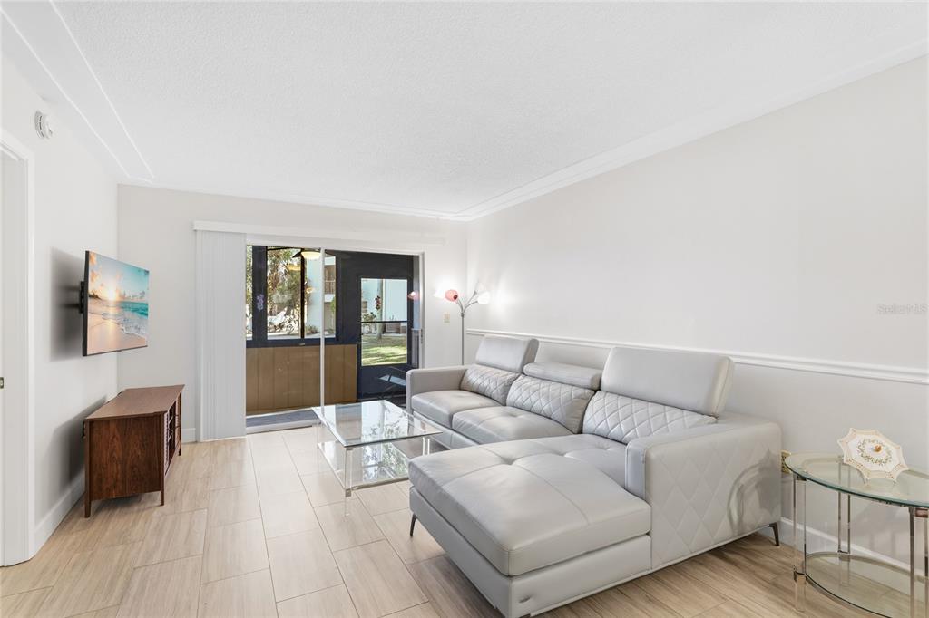 A living room features light tile flooring, a gray sectional sofa, and a glass coffee table — 2300 STICKNEY POINT ROAD UNIT 102, SARASOTA, FL