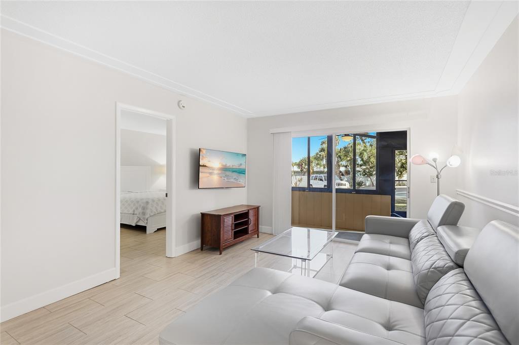 A living room features light tile flooring, a grey sectional sofa, and a sliding glass door — 2300 STICKNEY POINT ROAD UNIT 102, SARASOTA, FL