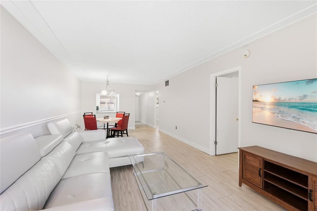A living room with a white sectional sofa, glass coffee table, and a dining area — 2300 STICKNEY POINT ROAD UNIT 102, SARASOTA, FL