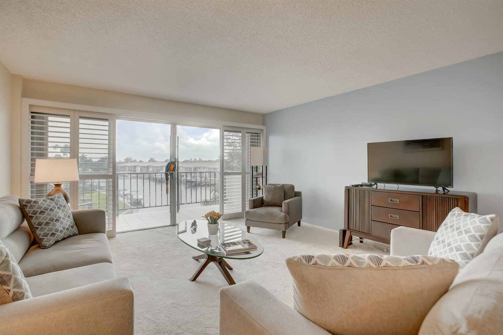 A living room with light carpet, neutral furniture, a glass coffee table, and a balcony view — 801 S Federal Highway # 308, Pompano Beach FL 33062, POMPANO BEACH, FL