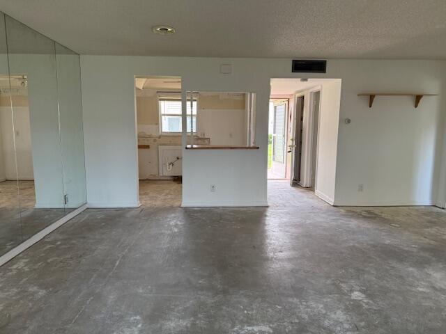 An unfurnished living area with concrete floors, a mirrored wall, and an open kitchen pass-through — 300 Bonnie Boulevard # 145, Palm Springs FL 33461, PALM SPRINGS, FL
