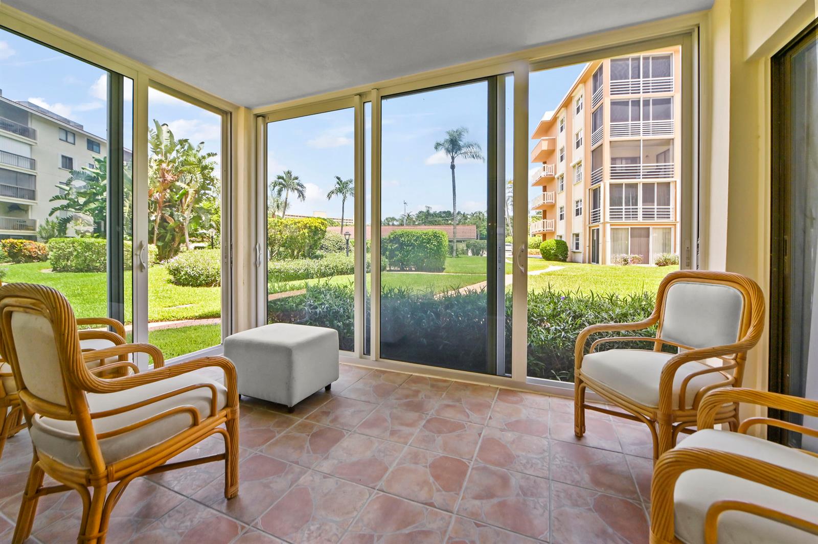 A sunroom with tile flooring and wicker chairs overlooks a grassy courtyard and apartment buildings — 308 Golfview Road # 101, North Palm Beach FL 33408, NORTH PALM BEACH, FL