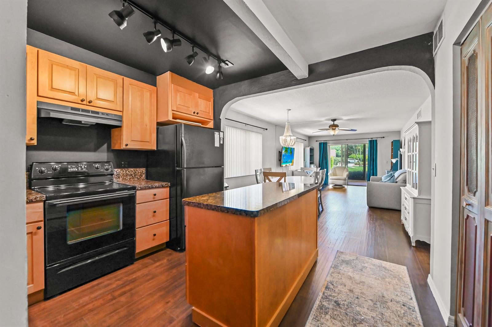 A kitchen with wood cabinets and black appliances opens into a living and dining area — 308 Golfview Road # 101, North Palm Beach FL 33408, NORTH PALM BEACH, FL