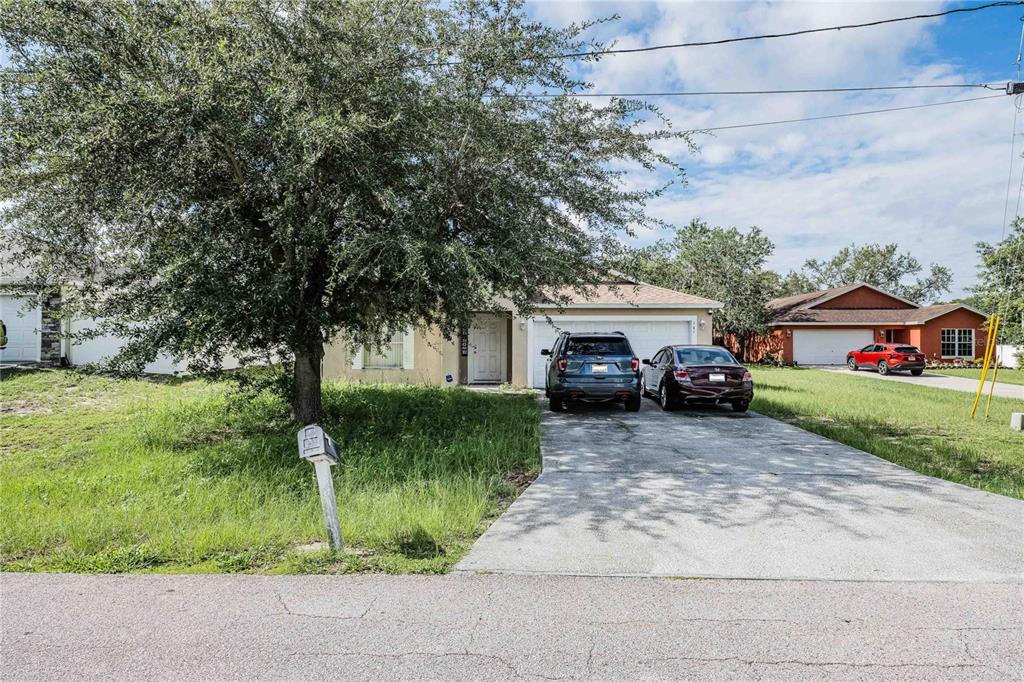 A single-story house with a concrete driveway, two parked cars, and a large front tree — 141 FLATFISH COURT, KISSIMMEE, FL