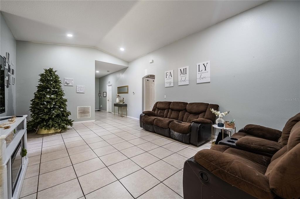 A living room features tile flooring, brown reclining sofas, and wall art spelling family — 141 FLATFISH COURT, KISSIMMEE, FL