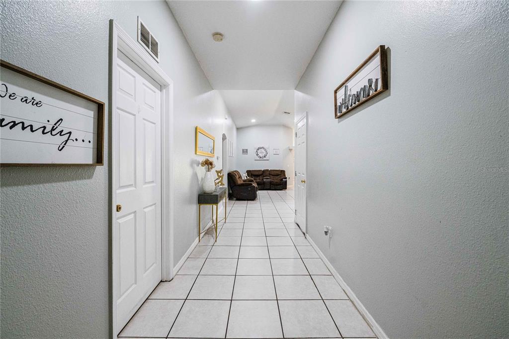 A tiled hallway leads from the foreground toward a living area with brown furniture — 141 FLATFISH COURT, KISSIMMEE, FL