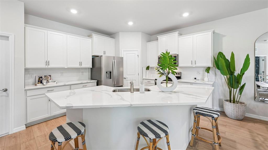 A modern kitchen features white cabinets, a marble-topped island, and light wood-look flooring — 18346 TAVERNSIDE TRAIL, LAKEWOOD RANCH, FL