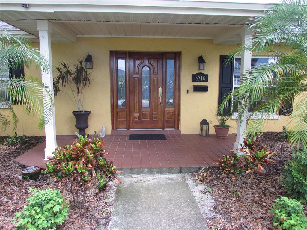 A yellow house exterior features a wooden front door with sidelights and a tiled porch — 5710 S BERNIE STREET, TAMPA, FL