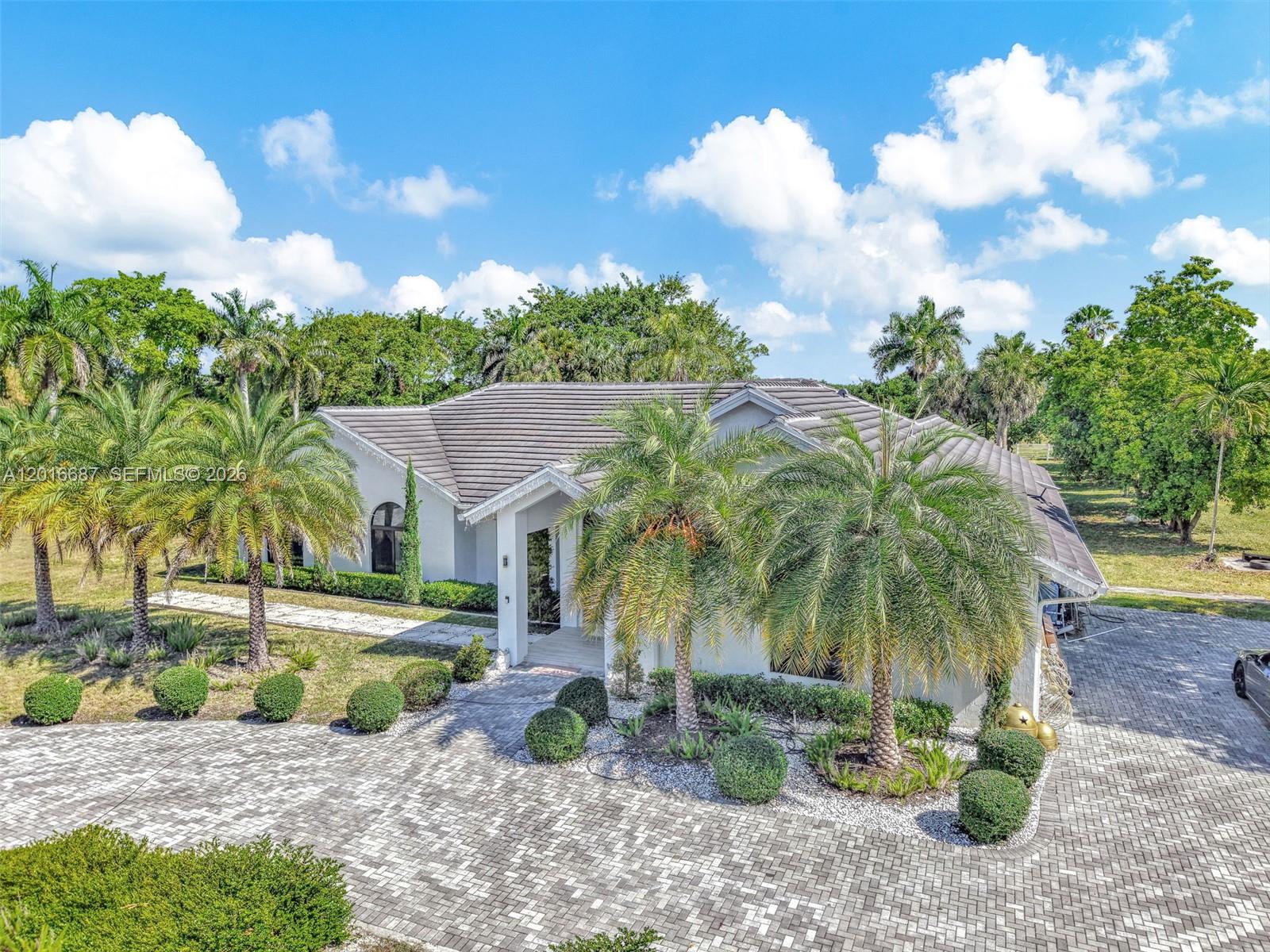 An exterior view of a single-story house with a paved driveway and palm trees — 17795 SW 158th St, Miami FL 33187, MIAMI, FL
