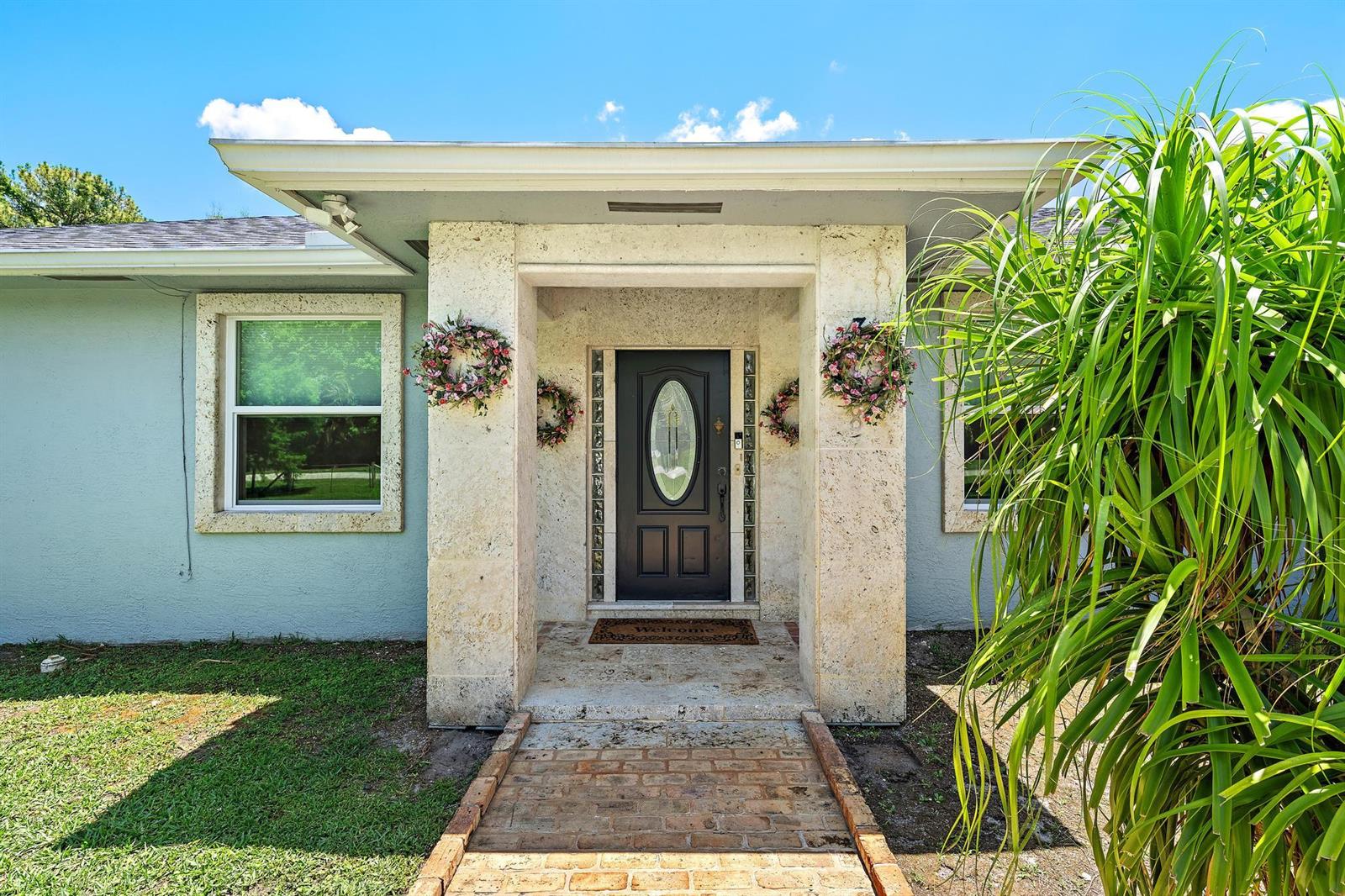 The exterior of a house features a stone-clad entryway with a dark front door — 13928 N 82nd Ln Lane N, FL 33412, FL