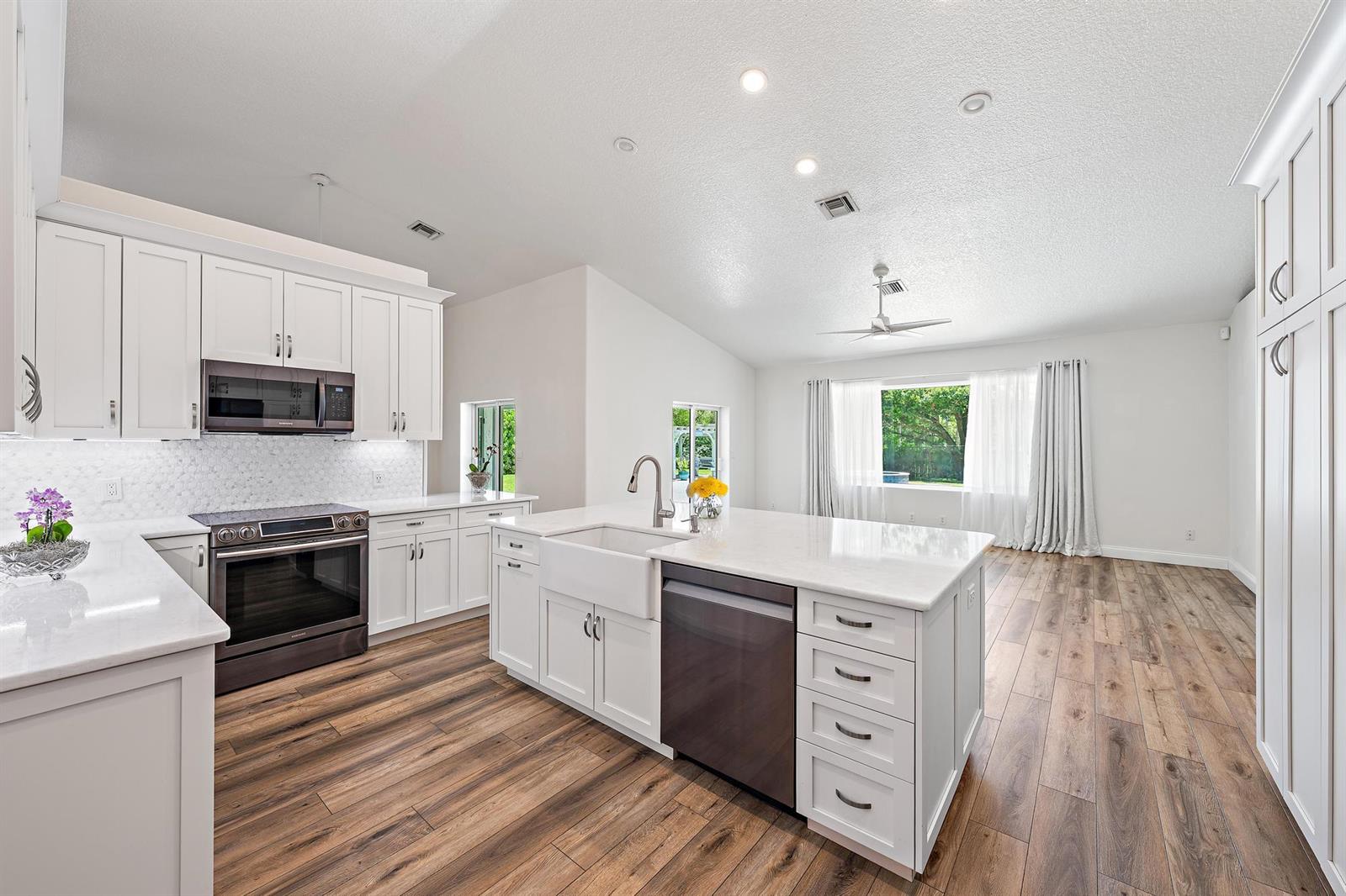 A modern white kitchen features a large island, stainless steel appliances, and wood-look flooring — 13928 N 82nd Ln Lane N, FL 33412, FL