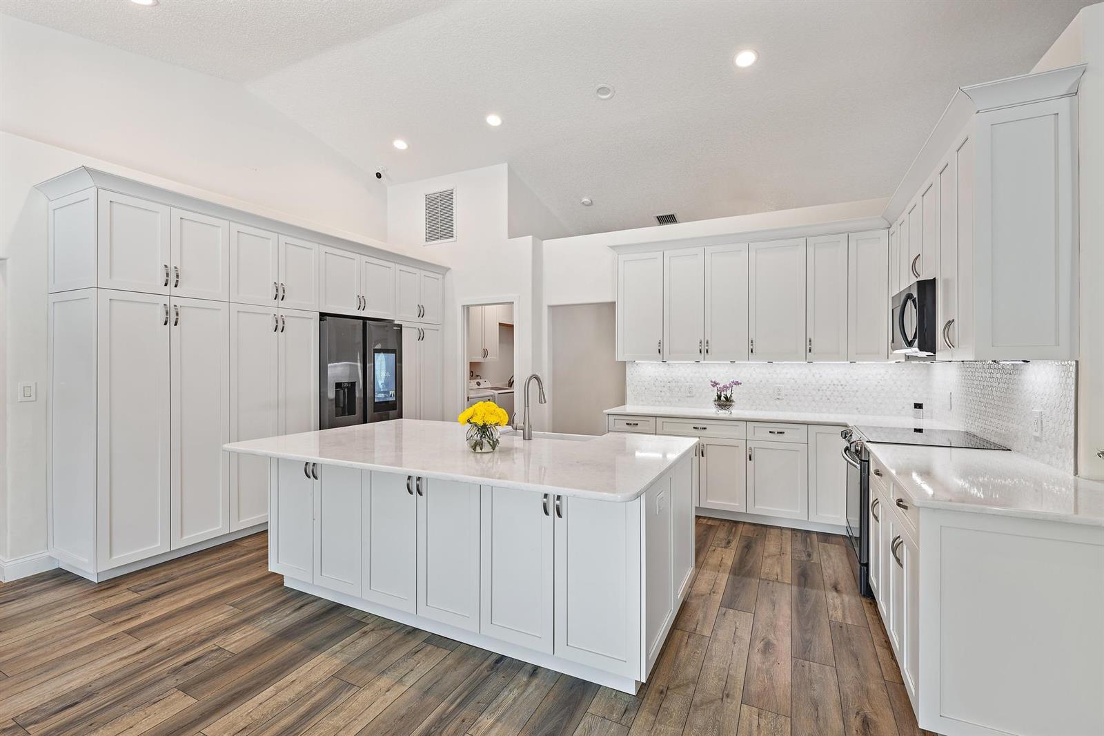 A modern kitchen features white cabinetry, a large central island, and wood-look flooring — 13928 N 82nd Ln Lane N, FL 33412, FL