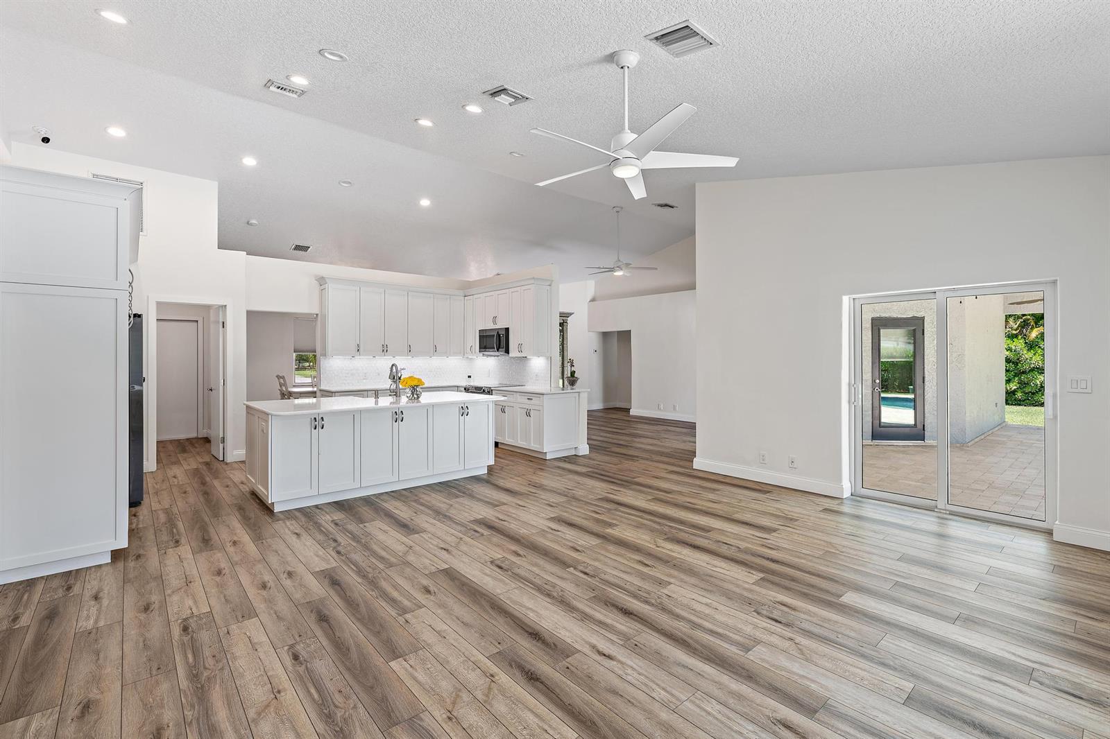 A bright, open-concept kitchen features white cabinetry, a central island, and wood-look flooring — 13928 N 82nd Ln Lane N, FL 33412, FL