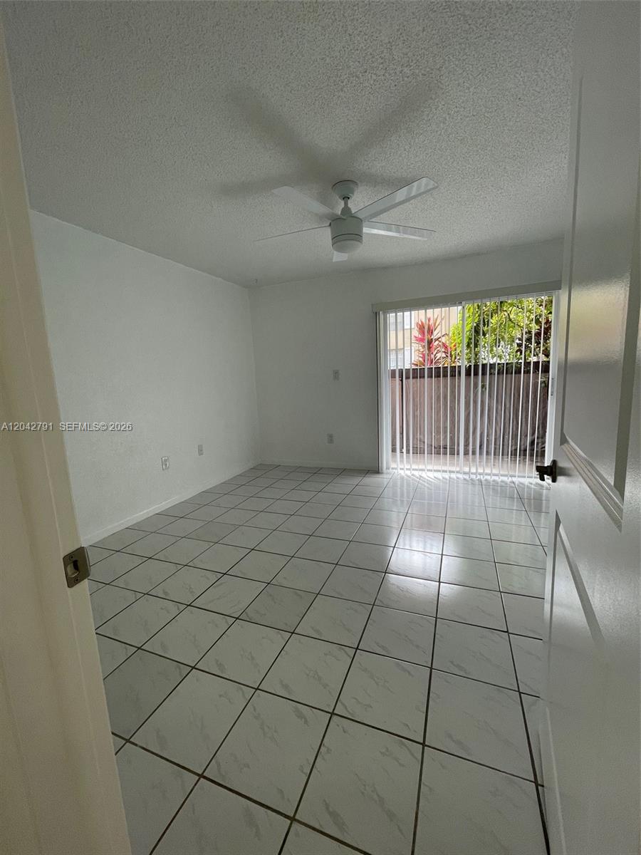 An empty room features white tile flooring, a ceiling fan, and sliding glass patio doors — 10832 SW 88th St # U13, Miami FL 33176, MIAMI, FL