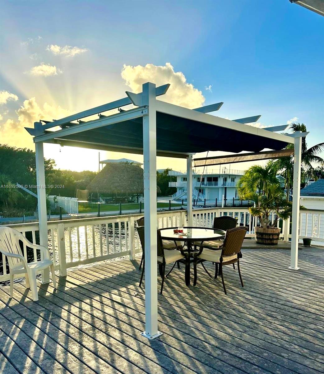 A white pergola with a canopy shades a patio table and chairs on a wooden deck — 72 Ocean Dr # 0, Key Largo FL 33037, KEY LARGO, FL
