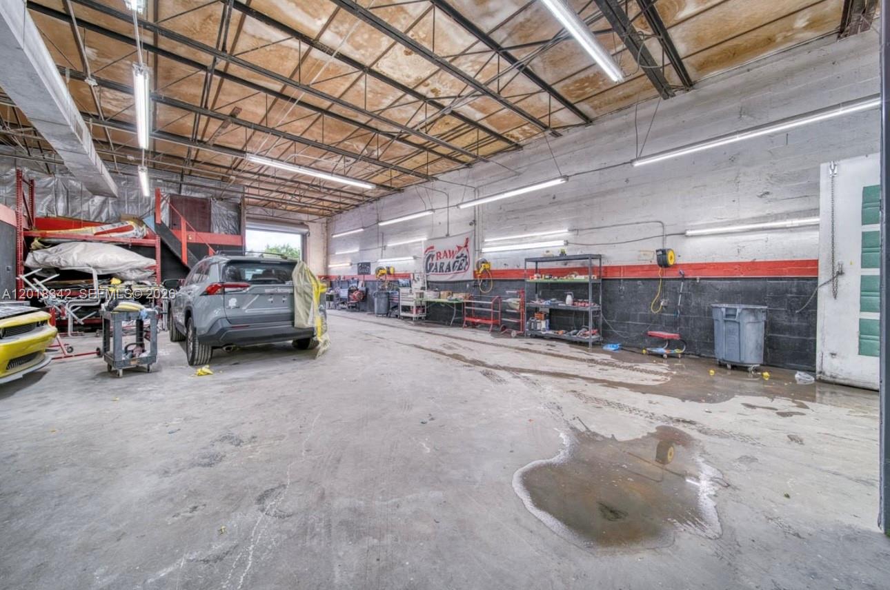 An industrial garage space features a concrete floor, exposed ceiling trusses, and fluorescent lighting — 3730 NW 82nd St, Hialeah FL 33147, HIALEAH, FL