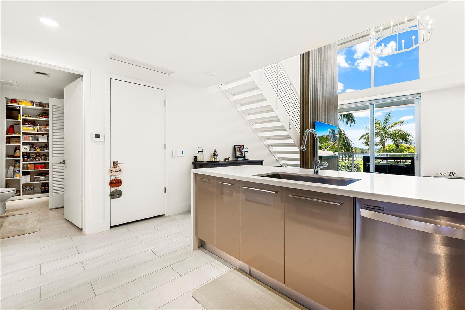 A modern kitchen features a beige island with a sink, white stairs, and a pantry — 2000 Metropica Way # 216, Sunrise FL 33323, SUNRISE, FL