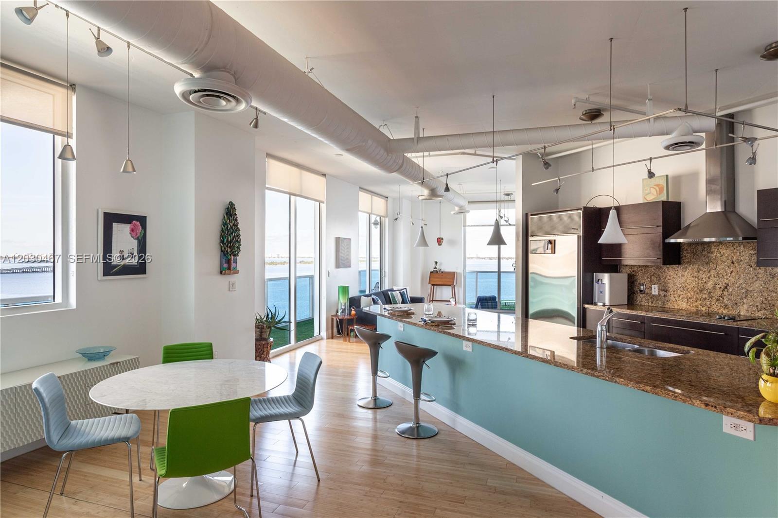 A modern kitchen and dining area features a teal island, granite countertops, and water views — 700 NE 25th St # 1003, Miami FL 33137, MIAMI, FL
