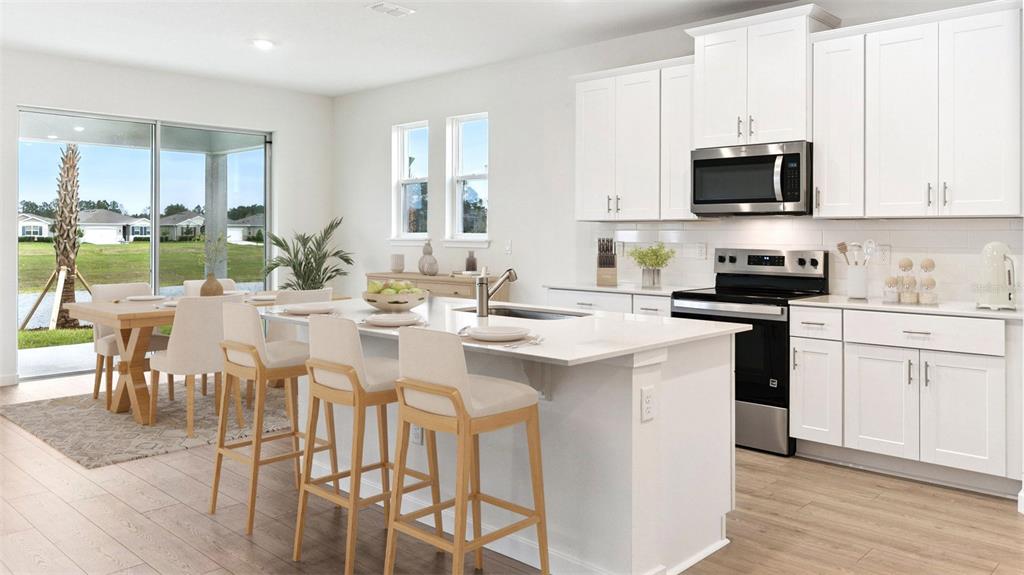 A bright kitchen features white cabinets, a central island with bar stools, and dining area — 300 BRACER WAY, ORMOND BEACH, FL