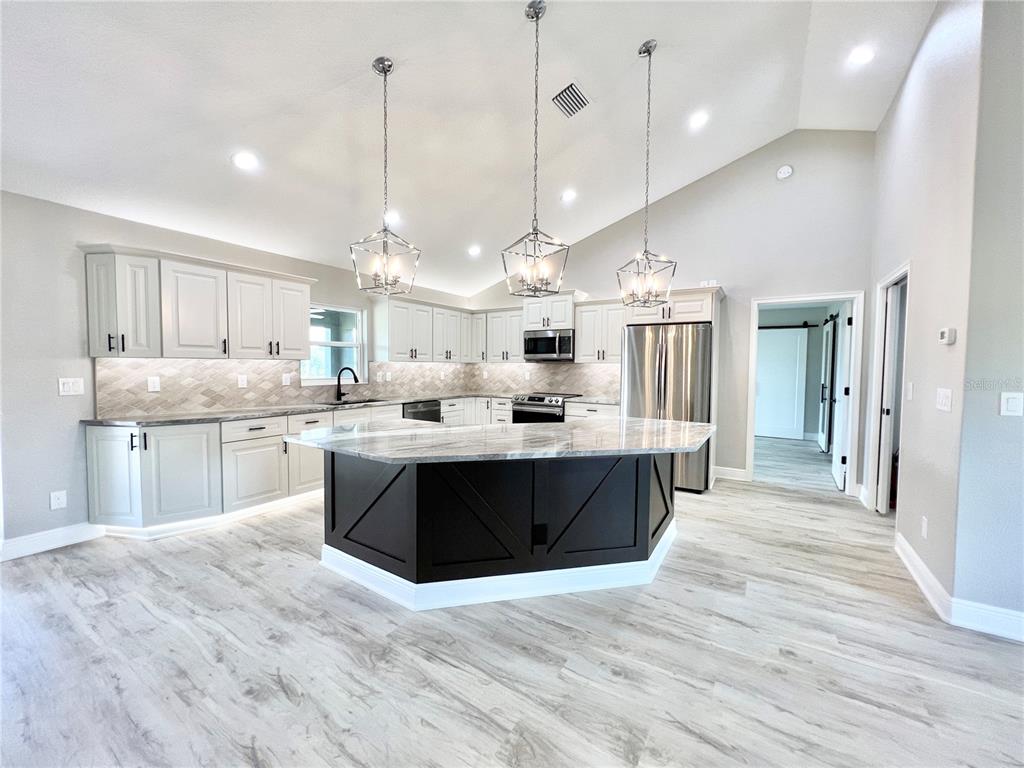 A kitchen features light gray cabinets, a dark island, and stainless steel appliances under vaulted ceilings — 6425 SW 180TH CIRCLE, DUNNELLON, FL