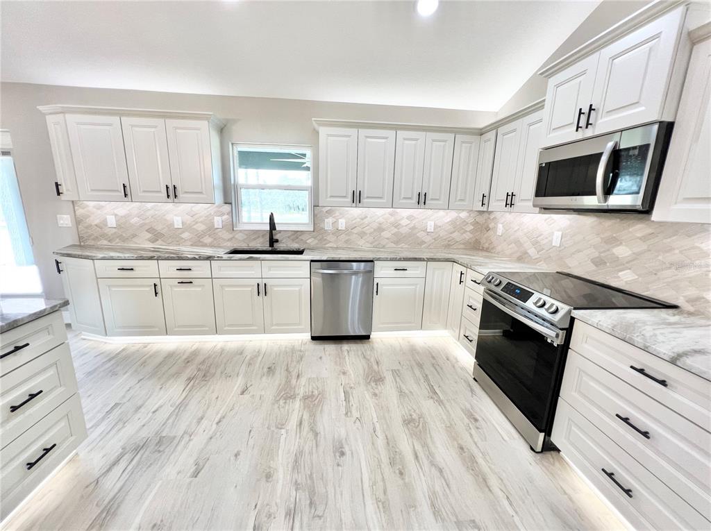 A modern kitchen features white cabinets, stainless steel appliances, and light wood-look flooring — 6425 SW 180TH CIRCLE, DUNNELLON, FL