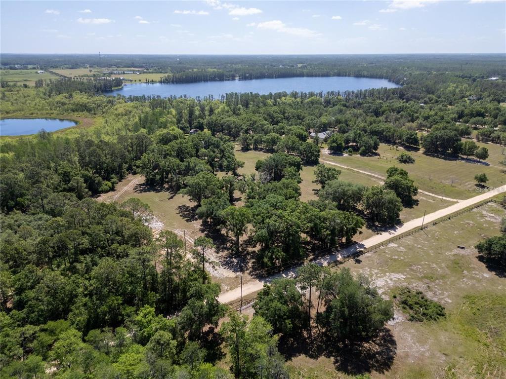 An aerial view shows a large, wooded property with a dirt road and a lake nearby — DR BAKER ROAD, GROVELAND, FL