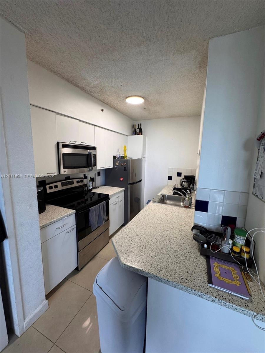 A galley-style kitchen features white cabinets, stainless steel appliances, and speckled granite countertops — 1500 Bay Rd # 1576S, Miami Beach FL 33139, MIAMI BEACH, FL