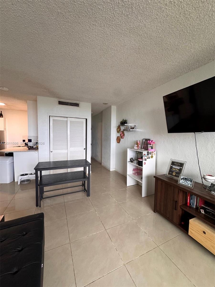 A living room features tile floors, a wall-mounted television, and a white storage shelf — 1500 Bay Rd # 1576S, Miami Beach FL 33139, MIAMI BEACH, FL