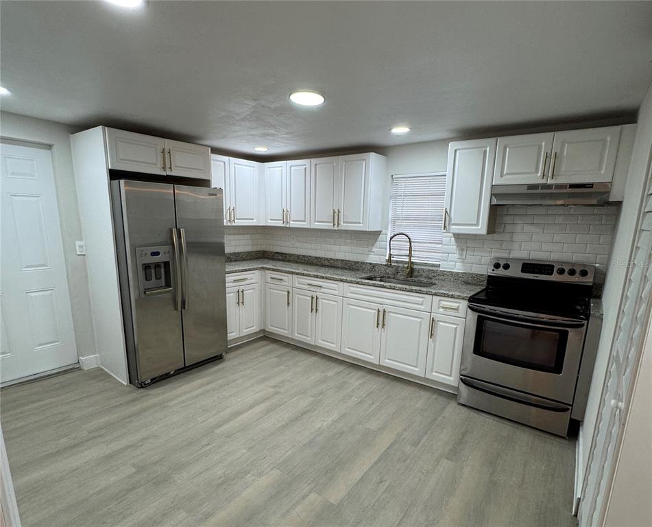 A kitchen features white cabinets, stainless steel appliances, a subway tile backsplash, and wood-look flooring — 8014 N ALASKA STREET, TAMPA, FL