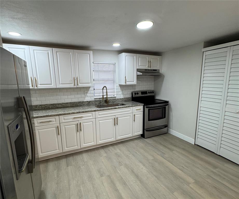 A kitchen features white cabinets, granite countertops, stainless steel appliances, and light wood-look flooring — 8014 N ALASKA STREET, TAMPA, FL