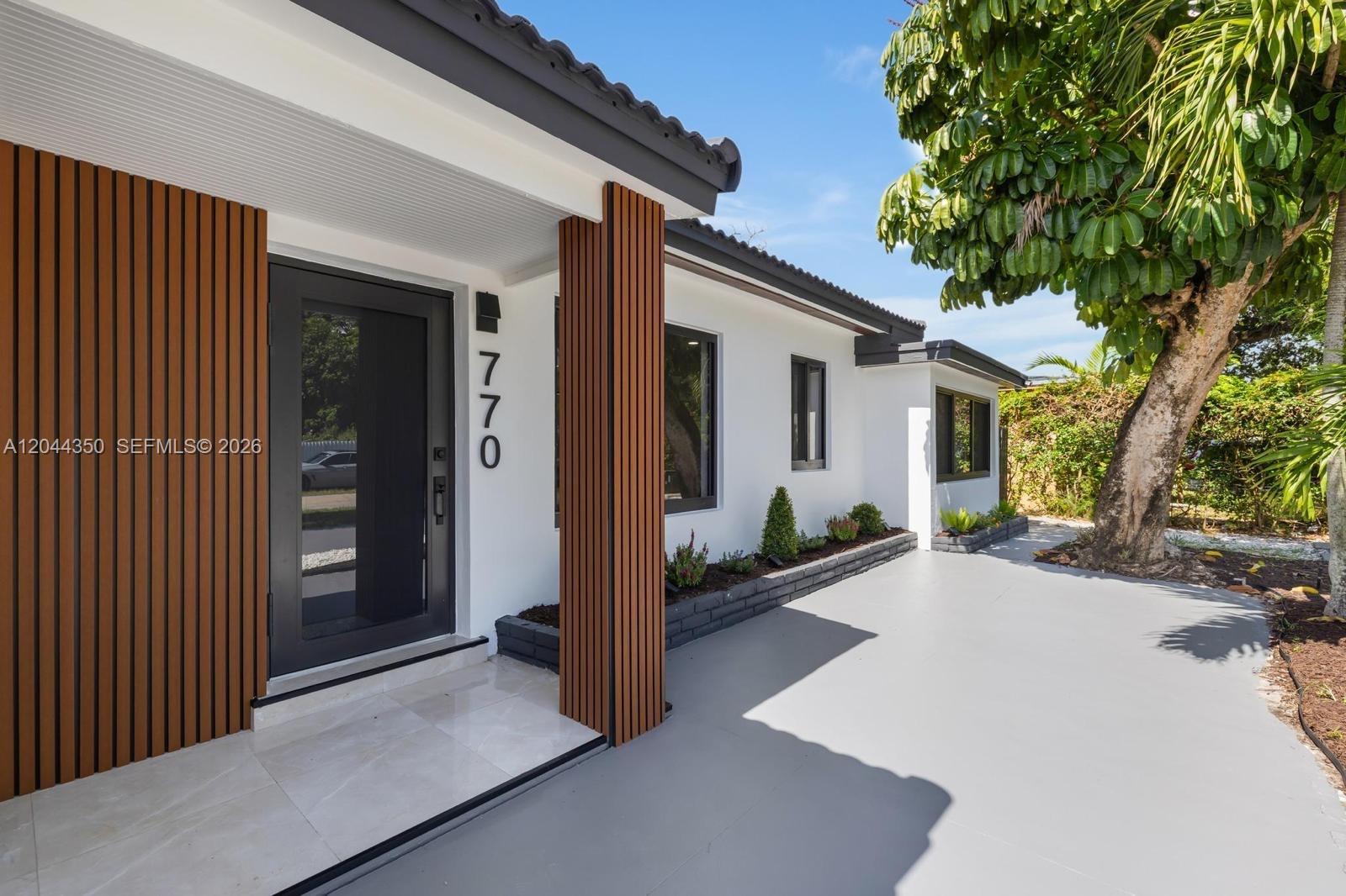 The exterior of a modern house features a dark door, wood-slat accents, and landscaping — 770 NE 160th St, Miami FL 33162, MIAMI, FL