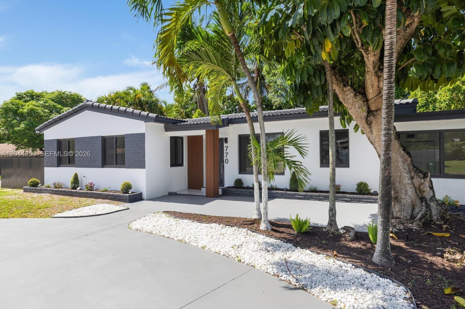 A white single-story house features a gray roof, dark trim, and a wood-slatted entryway — 770 NE 160th St, Miami FL 33162, MIAMI, FL