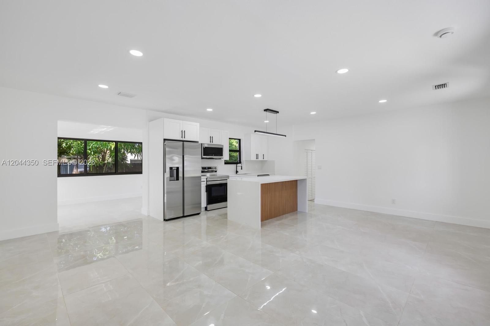 A modern kitchen features white cabinetry, stainless steel appliances, and a wood-slatted kitchen island — 770 NE 160th St, Miami FL 33162, MIAMI, FL