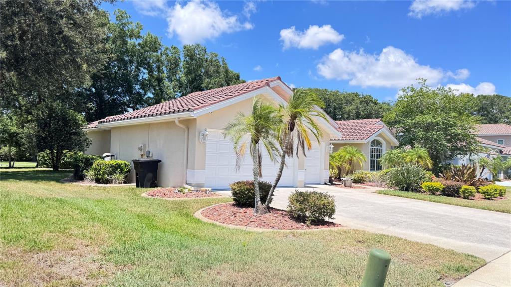 A single-story house with a tiled roof, tan stucco exterior, and landscaped front yard — 1230 BERKSHIRE LANE, TARPON SPRINGS, FL